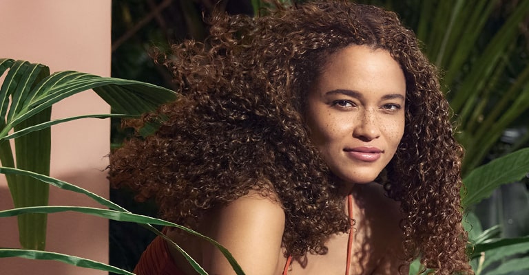 model with curly in hair in front of leaf background